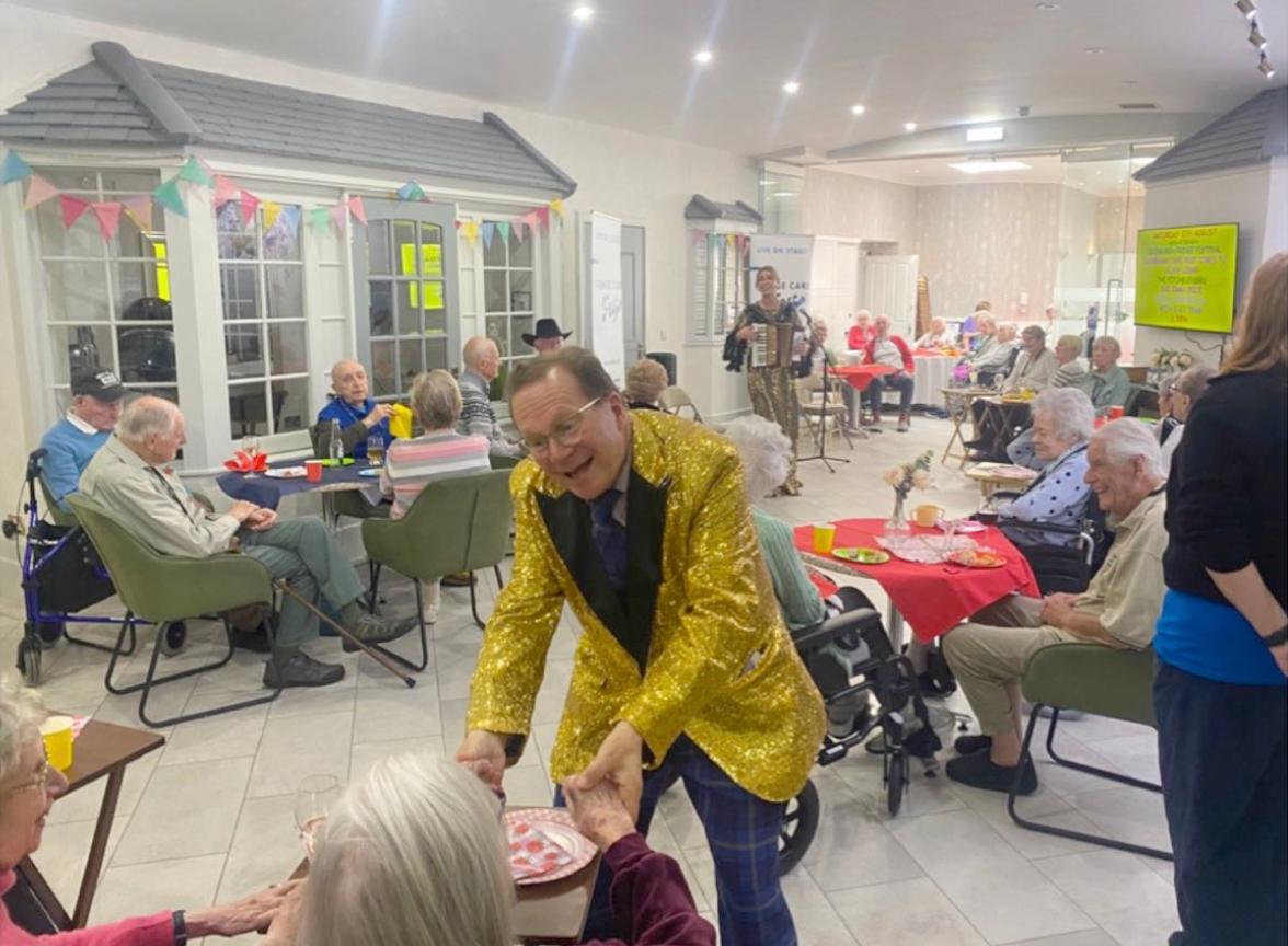 man in gold glittery jacket performs for care home residents